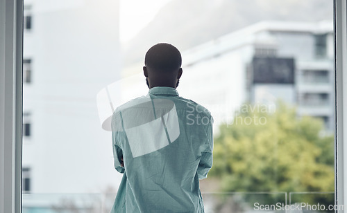 Image of Back, thinking and window with a business black man standing in his office looking at a city view. Idea, motivation and inspiration with a male employee at work, contemplating a decision in town