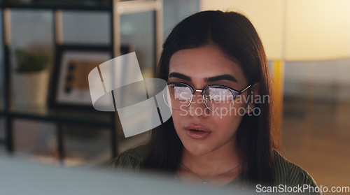 Image of Computer, night and professional with a woman editor working in an office at night for a journalism report. Face, editing and focus with a young journalist at work on a desktop for online content