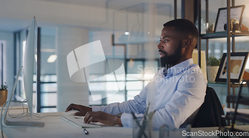 Image of Business man, focus and working on a computer at night while typing an email or report. A serious black male entrepreneur with technology for networking, internet connection and online research