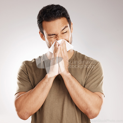 Image of Man sneezing, blowing nose and tissue with virus and health issue against a grey studio background. Male person, guy and model suffering from cold, sinus and hayfever with sickness and allergies