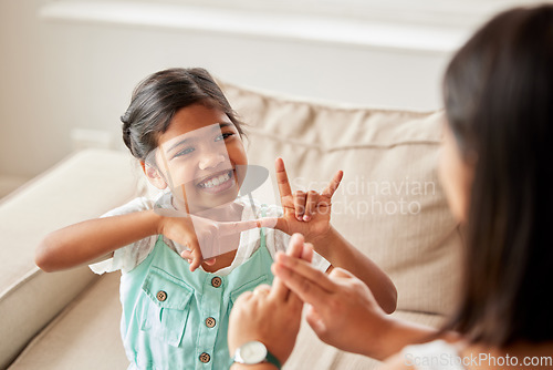 Image of Sign language, communication and child with her mother in the living room of their family home. Happy, smile and girl kid speaking with her hands to her deaf mom to communicate in their modern house.