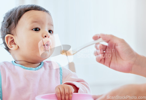 Image of Mother, feeding baby girl and spoon in home, kitchen or living room for nutrition, growth or health. Woman, hand and food for infant child for help, eating or balance in diet for development in house