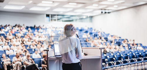 Image of Female speaker giving a talk on corporate business conference. Unrecognizable people in audience at conference hall. Business and Entrepreneurship event.