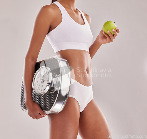 Image of Woman in underwear, body and apple with scale and lose weight, health with fitness and nutrition on studio background. Female model, healthy food and fruit with diet, detox and vegan lifestyle