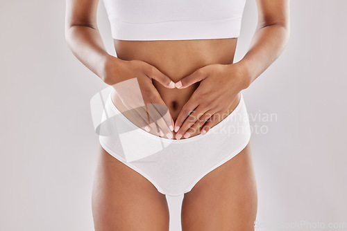 Image of Heart, hands and gut health by woman in lingerie in studio for digestion, wellness and diet on grey background. Lose weight, detox and finger emoji by female model in underwear for feminine hygiene