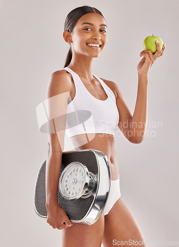 Image of Woman, body and apple with scale and lose weight, smile in portrait with health and nutrition on studio background. Happy female model, healthy food and fruit with diet, detox and vegan lifestyle