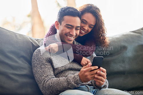 Image of Happy couple, phone and relax on sofa with social media, internet and online streaming service at home. Young interracial woman and man or partner on video call, connection or hug or love on couch