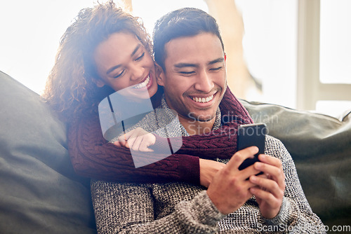 Image of Happy couple, phone and hug on couch with internet meme, reading news or online streaming service at home. Young interracial woman and man or partner on funny website, connection and love on sofa