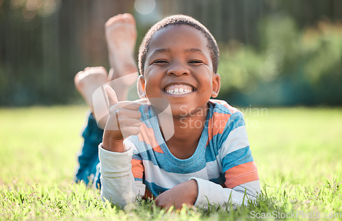 Image of Thumbs up, portrait of black boy and lying on grass in a nature park with a lens flare. Good news or thank you, success or winner and happy or excited young male child relaxing on a lawn outdoors