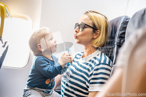 Image of Mom and child flying by plane. Mother holding and playing with her infant baby boy child in her lap during economy comercial flight. Concept photo of air travel with baby. Real people.