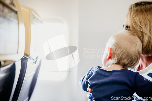 Image of Mom and child flying by plane. Mother holding and playing with her infant baby boy child in her lap during economy comercial flight. Concept photo of air travel with baby. Real people.