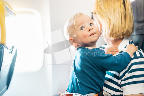 Image of Mom and child flying by plane. Mother holding and playing with her infant baby boy child in her lap during economy comercial flight. Concept photo of air travel with baby. Real people.