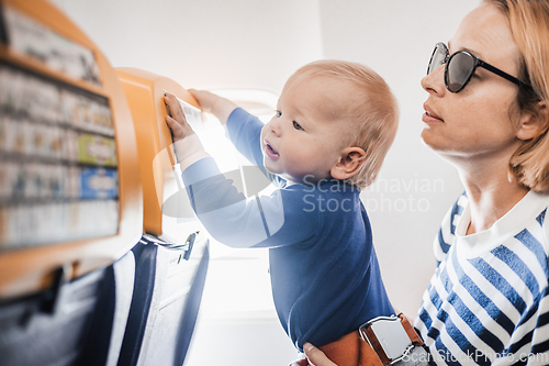 Image of Mom and child flying by plane. Mother holding and playing with her infant baby boy child in her lap during economy comercial flight. Concept photo of air travel with baby. Real people.