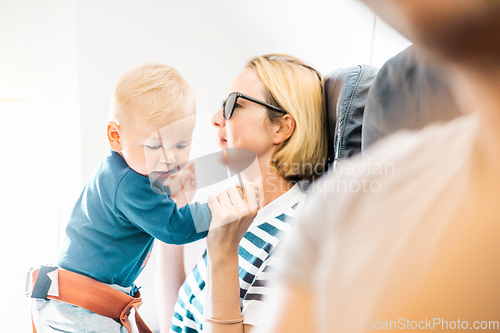 Image of Mom and child flying by plane. Mother holding and playing with her infant baby boy child in her lap during economy comercial flight. Concept photo of air travel with baby. Real people.