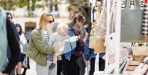 Image of Mother walking carrying his infant baby boy child in crowd of people wisiting sunday flea market in Malaga, Spain