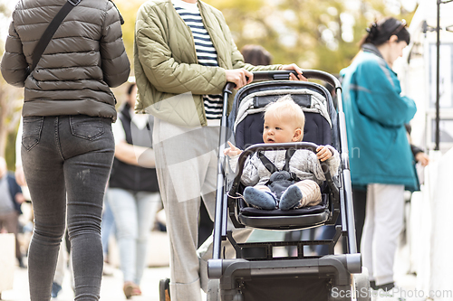 Image of Mother walking and pushing his infant baby boy child in stroller in crowd of people wisiting sunday flea market in Malaga, Spain.