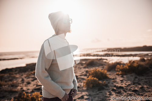 Image of Portrait of young stylish woman wearing wool sweater, wool cap and sunglasses on long sandy beach in spring