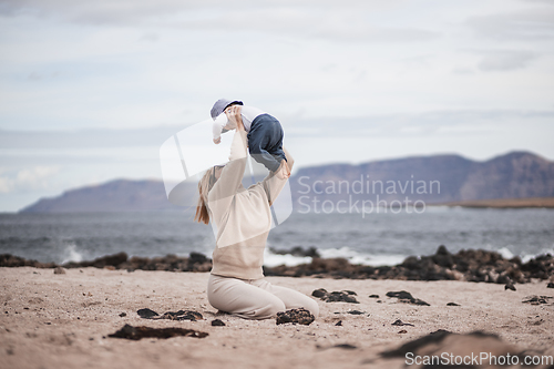 Image of Mother enjoying winter vacations holding, playing and lifting his infant baby boy son high in the air on sandy beach on Lanzarote island, Spain. Family travel and vacations concept