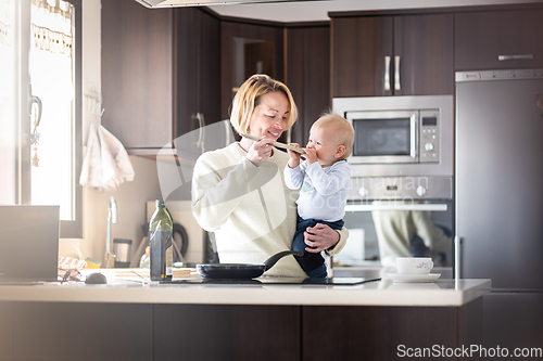 Image of Happy mother and little infant baby boy cooking and tasting healthy dinner in domestic kitchen. Family, lifestyle, domestic life, food, healthy eating and people concept.