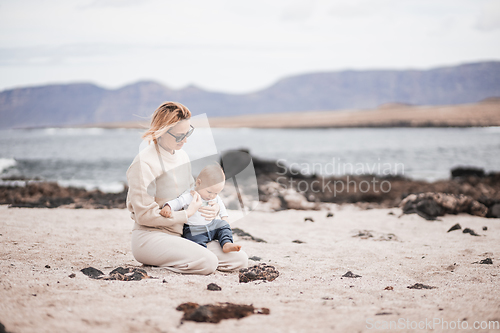 Image of Mother enjoying winter beach vacations playing with his infant baby boy son on wild volcanic sandy beach on Lanzarote island, Canary Islands, Spain. Family travel and vacations concept