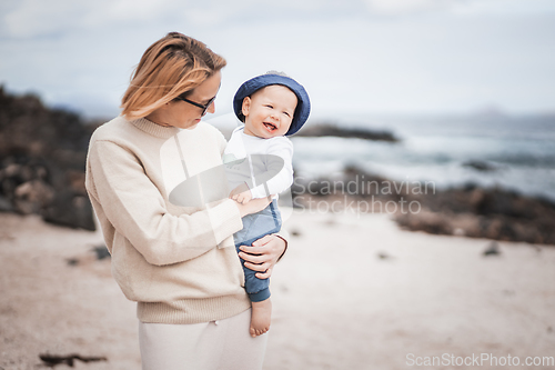 Image of Mother enjoying winter vacations holding and playing with his infant baby boy son on volcanic sandy beach on Lanzarote island, Spain. Family travel and vacations concept