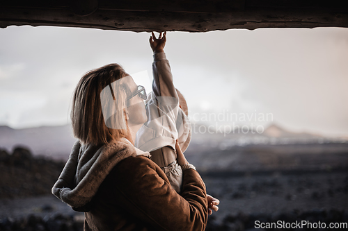 Image of Mother enjoying winter vacations playing with his infant baby boy son on black sandy volcanic beach of Janubio on Lanzarote island, Spain on windy overcast day. Family travel vacations concept.