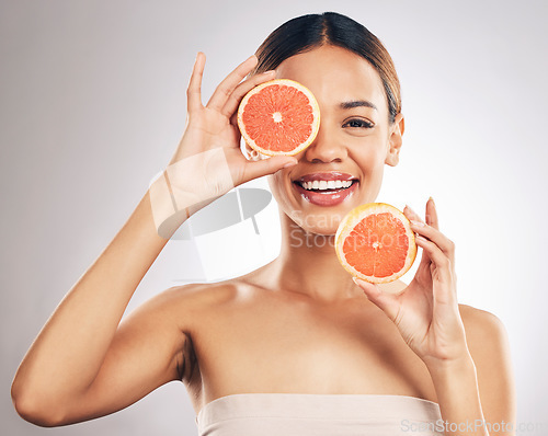 Image of Portrait, skincare and happy woman with grapefruit in studio fo organic, cosmetic or treatment on grey background. Citrus, face and female model with fruit for eco, vegan or skin detox with vitamin c