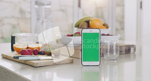 Image of Phone, green screen and kitchen with fruit, diet app and table by blurred background in home for smoothie. Smartphone, counter and fruits with space for mock up, logo and nutrition brand in house