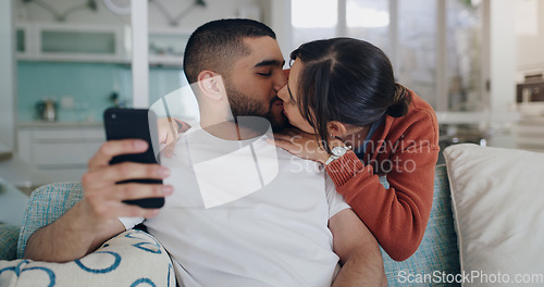 Image of Love, kiss and couple on sofa with phone, embrace and surfing social media post or or streaming online. Cellphone, man and woman on couch, kissing and hugging in romantic relationship in living room.