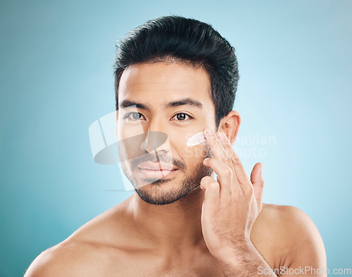 Image of Wellness, skincare and man with face cream in a studio for a natural, moisturizing and health routine. Male model with facial spf, lotion or moisturizer for dermatology treatment by a blue background