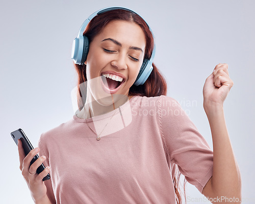 Image of Happy woman with mobile in headphones singing music or dancing to radio audio in studio on white background. Dance, smile or girl streaming or listening to song playlist in freedom with cellphone