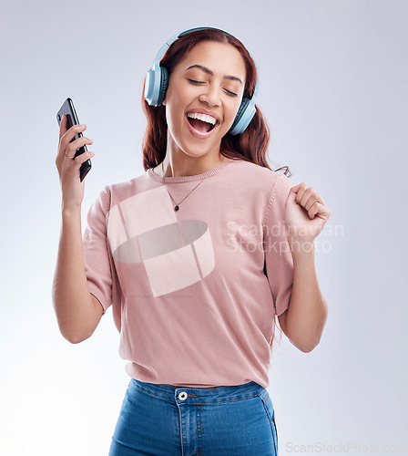 Image of Happy girl with mobile in headphones dancing music or singing a radio audio in studio on white background. Dance, smile or woman streaming or listening to song playlist in freedom with cellphone