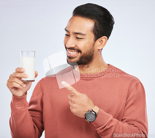 Image of Man pointing at milk, drink and health with nutrition, calcium and vitamins with vanilla shake isolated on studio background. Male person with smile, promote dairy product in glass and healthy life