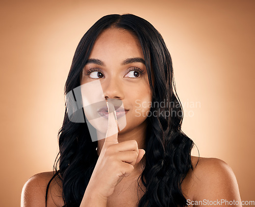 Image of Beauty, secret and woman with hand on face in studio for makeup, cosmetics or dermatology care. Spa, salon or luxury skincare or facial, cosmetic treatment or fingers on lips on brown background