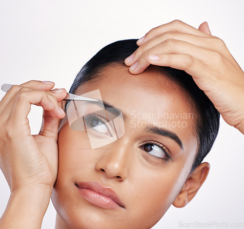 Image of Face, woman and plucking eyebrows with tweezers in studio for self care and hair removal. Headshot of natural model person with beauty tools in hand for cleaning and grooming on a white background