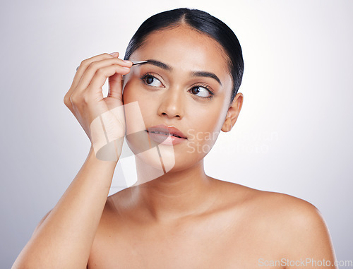 Image of Face, woman with tweezers and makeup against a studio background. Cosmetics or dermatology, skincare or beauty treatment and female person shaping her eyebrows for facial care against backdrop