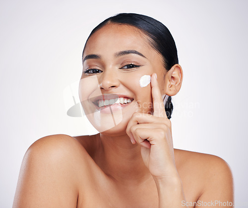 Image of Woman in portrait, lotion on face and beauty with skincare, smile and moisturizer isolated on studio background. Happy female model apply cream, dermatology and cosmetic product with skin glow