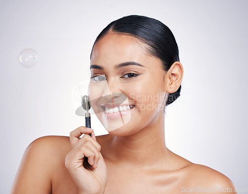 Image of Smile, face roller and portrait a woman in studio for beauty glow, dermatology or natural cosmetics. Happy aesthetic model with tools for a facial massage and skincare results on a white background