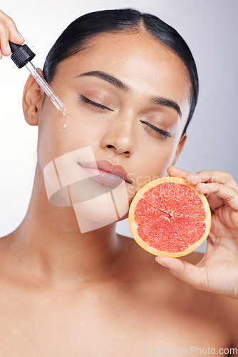 Image of Woman, face and serum with beauty and grapefruit, skincare oil with natural cosmetics isolated on studio background. Fruit, female model with pipette and vitamin c acid for skin with dermatology