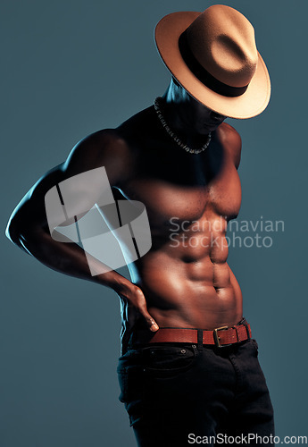 Image of Black man, topless and sexy fashion model with abs, cow boy style with hat isolated on blue background. Dark, shadow and body with muscular male person, pose with six pack and stylish in studio