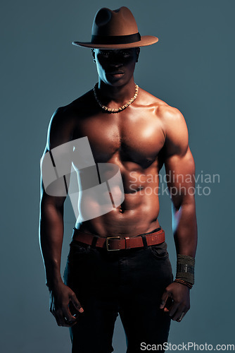 Image of Black man, shirtless with strong fashion model and sexy, cow boy style with hat isolated on blue background. Dark, shadow and body with muscular male person, pose with six pack and stylish in studio