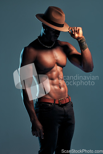 Image of Black man, shirtless and sexy fashion model with abs, cow boy style with hat isolated on blue background. Dark, shadow and body with muscular male person, pose with six pack and stylish in studio