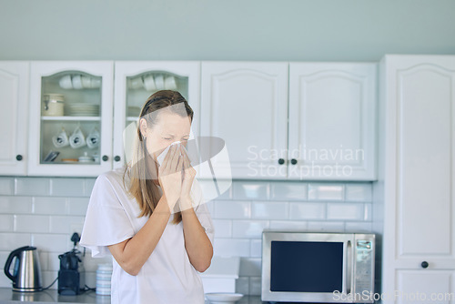 Image of Allergies, toilet paper and woman blowing her nose in the kitchen for a cold, flu or sneeze at her home. Illness, virus and young female person with tissue for sinus, hay fever or covid in apartment.