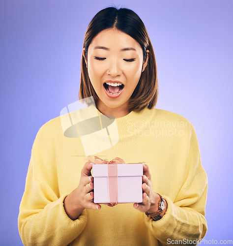 Image of Happy, surprise and woman with a gift in a studio for birthday celebration with a wow face. Happiness, excited and Asian female model with a present, box or package isolated by a purple background.