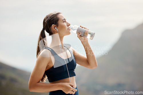 Image of Fitness, woman with earphones, drinking water and hiking in nature for health and wellness during exercise. Music, bottle and fit girl on hike in park for body workout with radio streaming or podcast