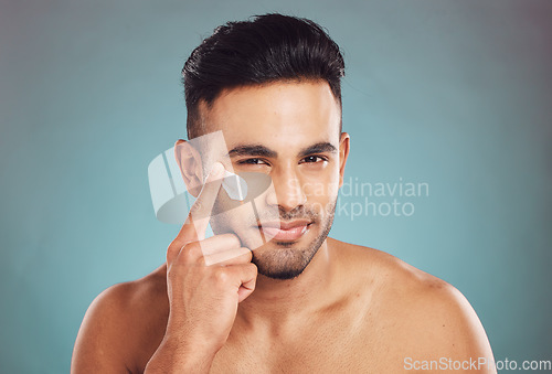 Image of Portrait, beauty and lotion with a man in studio on a gray background to apply antiaging facial treatment. Face, skincare and cream with a young male person indoor for wellness or aesthetic self care