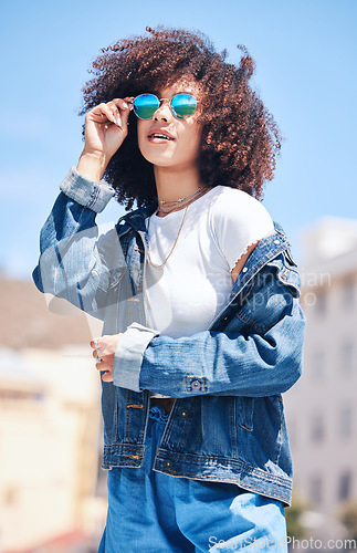 Image of Woman, fashion and sunglasses outdoor in city for streetwear, summer and travel on a street. African person with natural hair or afro and urban background, glasses and jeans or clothes for freedom