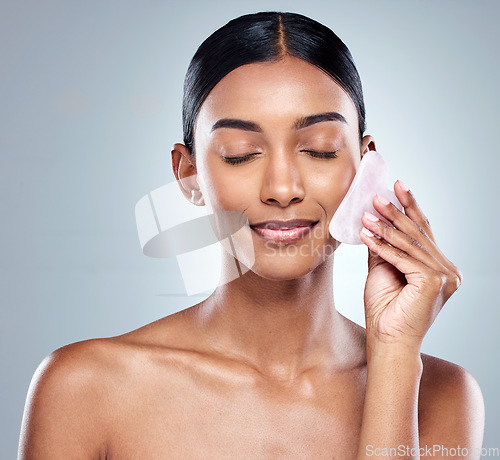 Image of Beauty, skincare and gua sha with face of woman in studio for massage, wellness and cosmetics. Spa, self care and glow with model on grey background for facial, cosmetology and rose quartz crystal