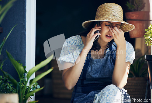 Image of Mental health, woman florist with headache and with smartphone on a phone call with a client at her workplace. Anxiety or stress, sad and female person talking on a cellphone for customer service.