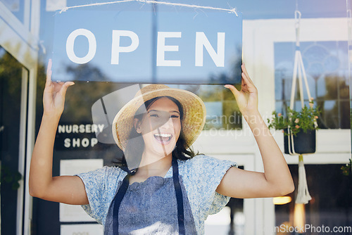 Image of Portrait, nursery and open with a woman hanging a sign in the window of her shop for gardening. Small business, garden center and an excited young female entrepreneur opening her new flower store